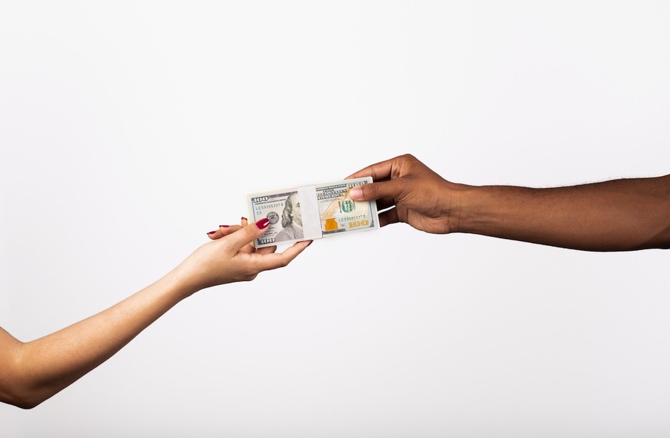 Two outreached hands appear from opposite directions, holding a stack of $100 bills.