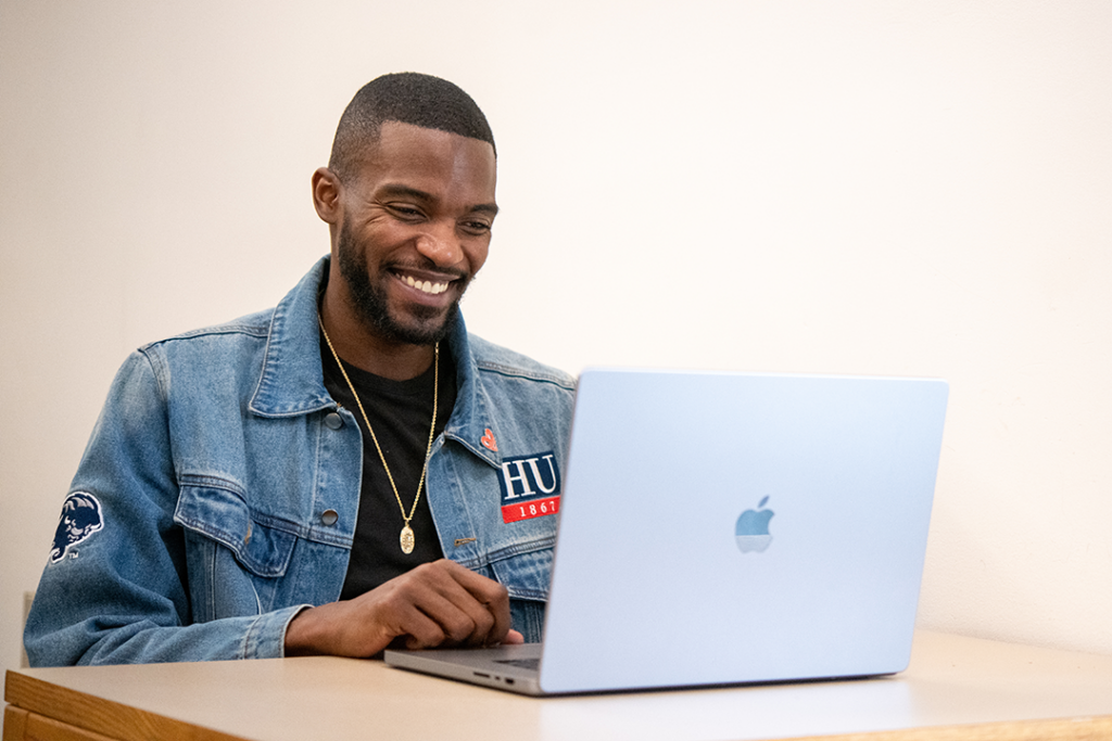 A smiling Howard University student works at a laptop computer.