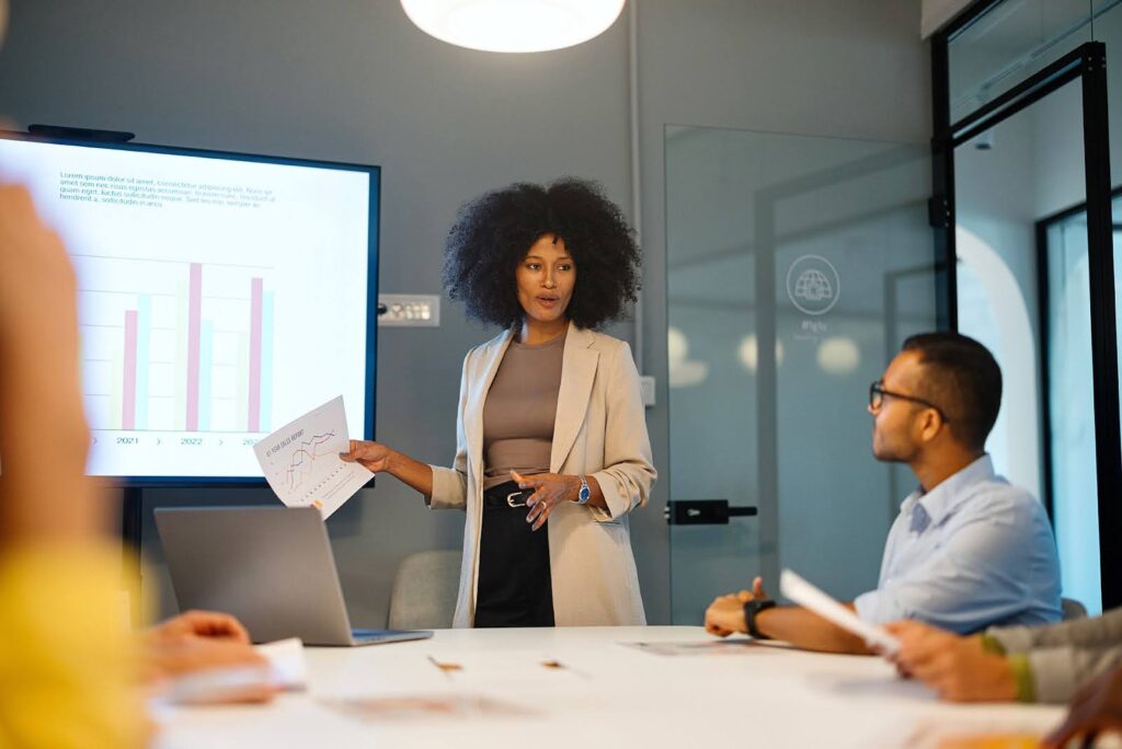 In a conference room, a business professional presents data on a large screen to team members.