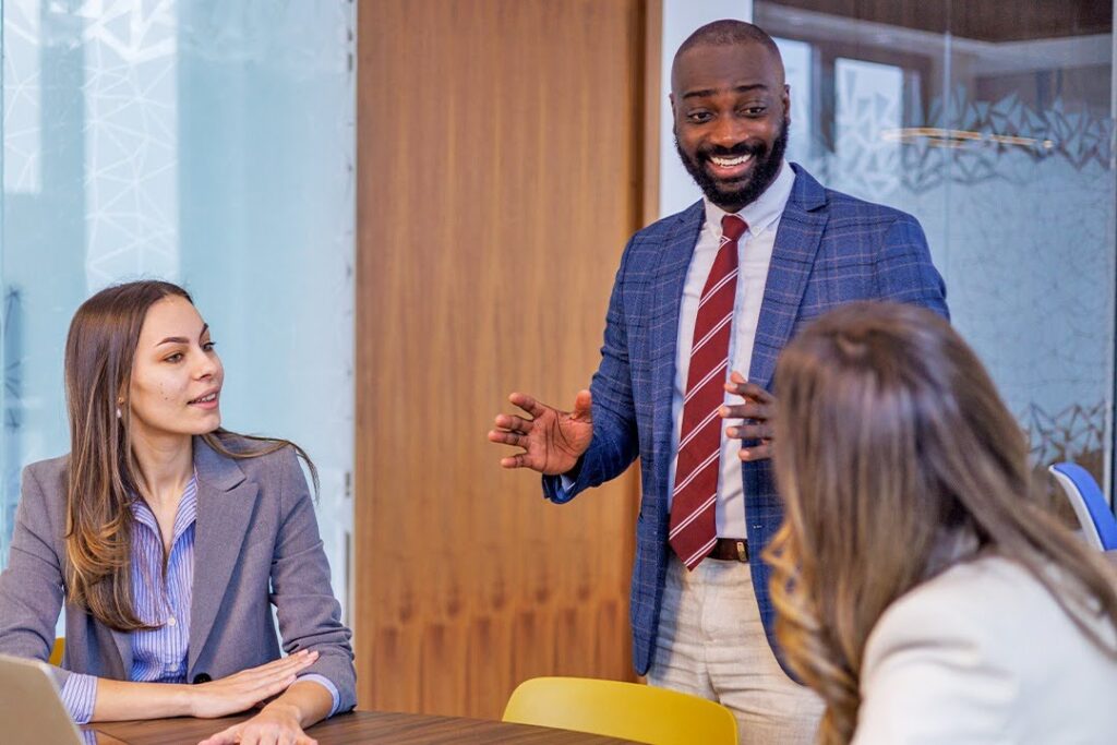 Professional meeting with one person presenting to two colleagues at a table.
